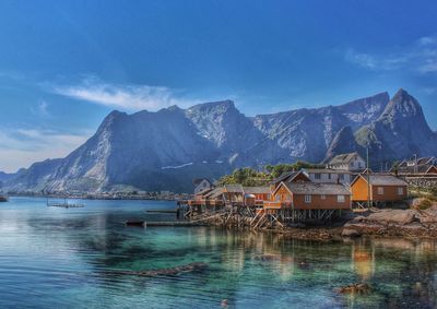 Stilt houses by lake against rocky mountains and sky on sunny day