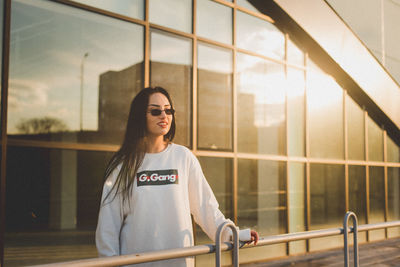 Young woman looking away while standing against window