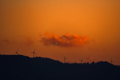 Silhouette of wind turbines on field against orange sky