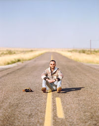 Portrait of man sitting on road against sky