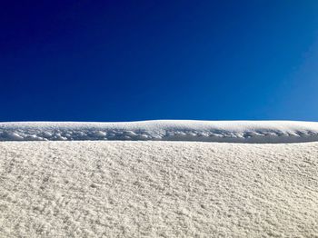 Snow covered landscape against clear blue sky