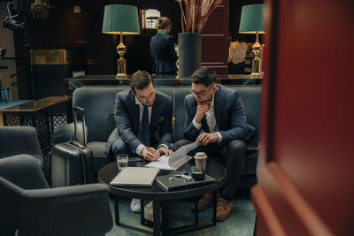 Young businesswoman signing contract while sitting my male colleague in hotel lounge