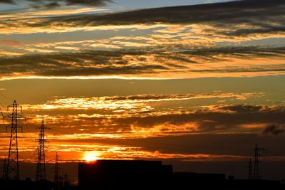 Silhouette electricity pylon against dramatic sky during sunset