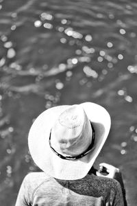 Rear view of person wearing hat sitting against water