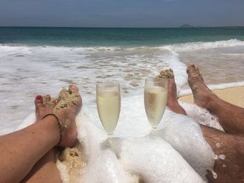 Low section of couple with drinks on beach