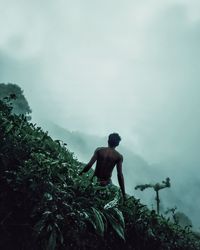 Rear view of shirtless man looking at mountain against sky