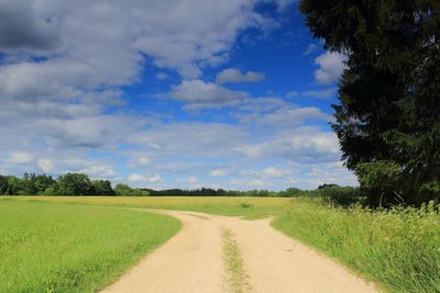 Dirt road amidst field against sky