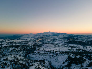 Aerial view of snow covered landscape against clear sky during sunset