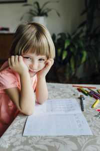 Portrait of bored girl looking at camera while doing homework