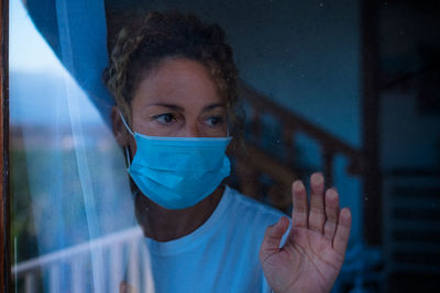 Close-up of woman wearing mask seen through window