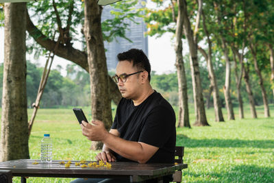 Young man using smart phone while sitting on tree