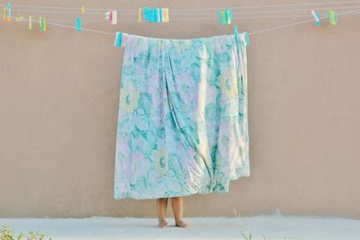 Young child hanging floral bedsheet to dry outside