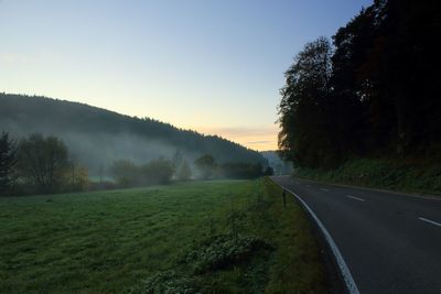 Road amidst trees against sky during sunset