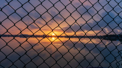 Chainlink fence against lake during sunset