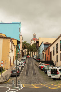 Cars on road by buildings against sky