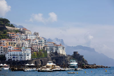 Sailboats in sea by buildings against sky