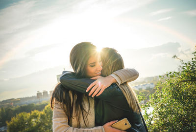 Woman embracing friend against sky