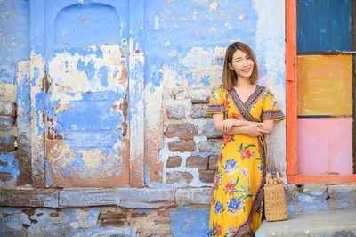 Portrait of smiling young woman standing against wall