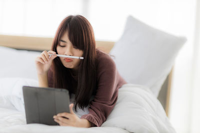 Young woman using mobile phone while sitting on bed