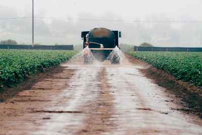 Water spraying on dirt road from truck in farm