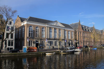 Boats moored in canal by buildings against sky