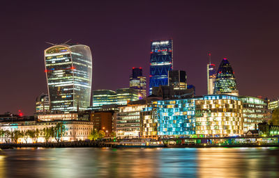 Illuminated buildings by river against sky in city at night