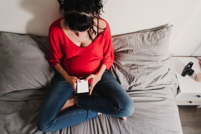 High angle view of woman using phone while sitting on bed at home