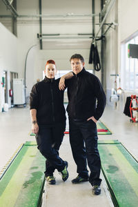Full length portrait of confident mechanics standing in auto repair shop