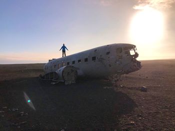 Woman standing on abandoned airplane against sky during sunset