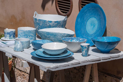 Blue and white ceramic plates, vases, and cups displayed on a wooden table outdoors.