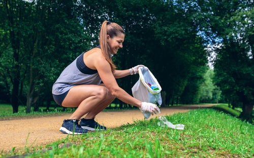 Full length of woman picking up garbage on grass against trees