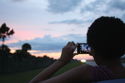 Rear view of woman photographing sky during sunset on field