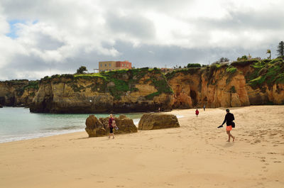 People walking at beach against cloudy sky