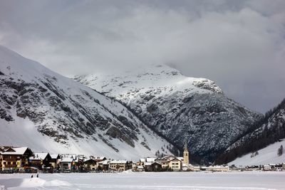 Snow covered houses by mountain against sky