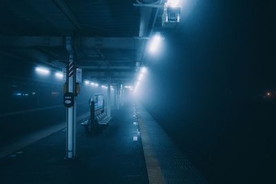 Illuminated railroad station platform at night in foggy weather