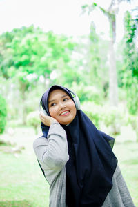 Portrait of smiling young woman standing against trees