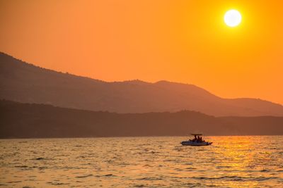 Silhouette boat sailing on sea against orange sky