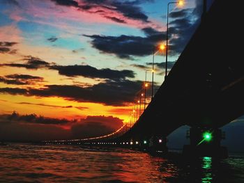 Illuminated bridge over sea against sky at night