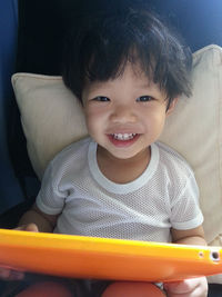 Close-up portrait of happy boy using digital tablet while sitting on chair