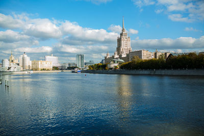View of buildings by river against cloudy sky