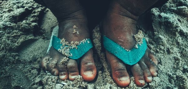 Low section of man wearing flip-flop on sand