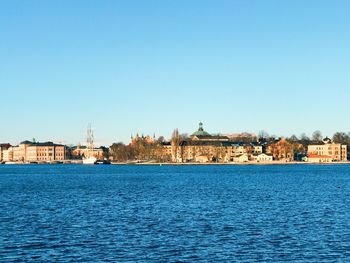 Buildings by river against clear blue sky