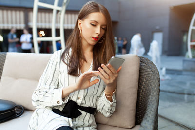Young woman using mobile phone while sitting in laptop
