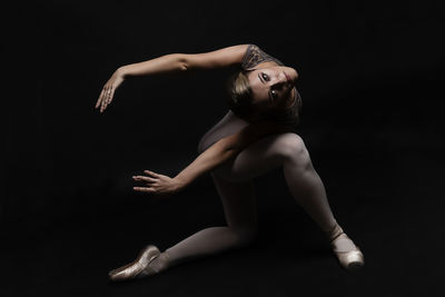 Portrait of ballet dancer stretching exercising kagainst black background