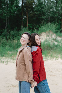 Two young caucasian young women friends standing back to back and laughing. real friensgip concept.