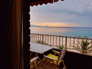 Chairs and table by sea against sky during sunset