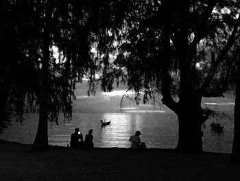 Silhouette people sitting on tree by sea