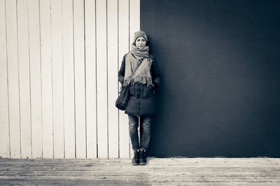 Woman with hands in pocket standing against wall