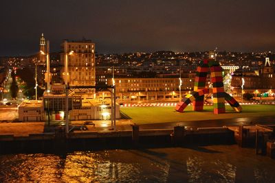 Illuminated buildings by river against sky in city at night