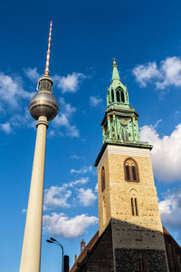 Low angle view of fernsehturm and cathedral against cloudy sky